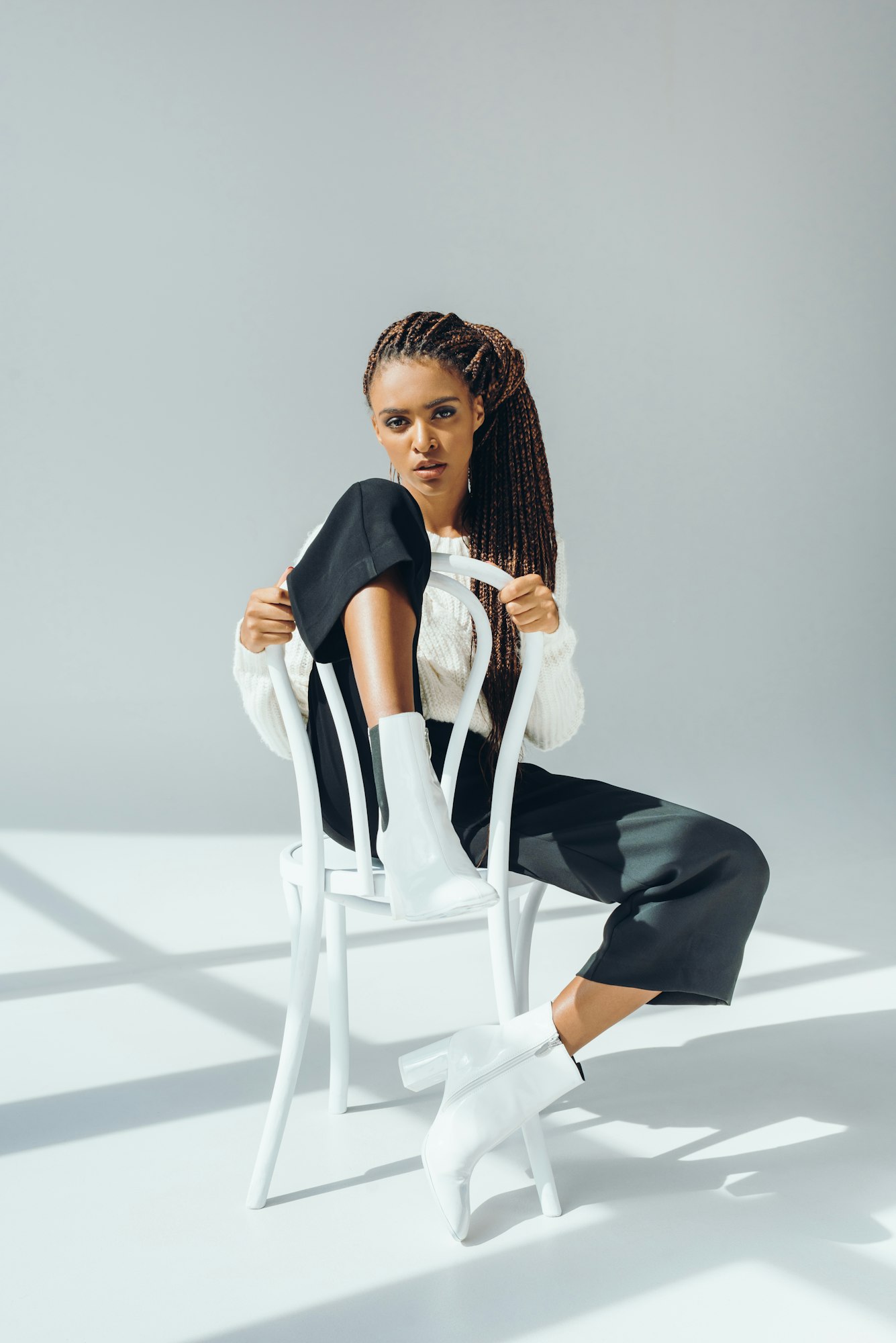 beautiful african american girl in trendy winter outfit sitting on chair and looking at camera